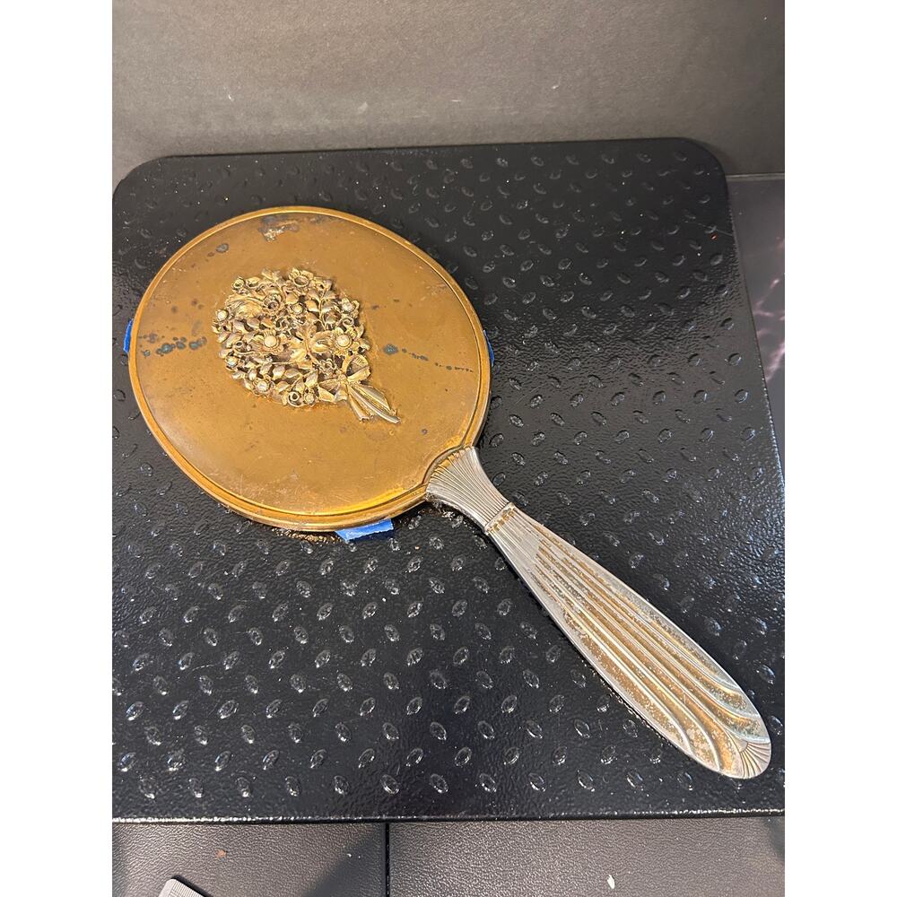 antique hand mirror with floral filigree crest on a polished gold-tone back